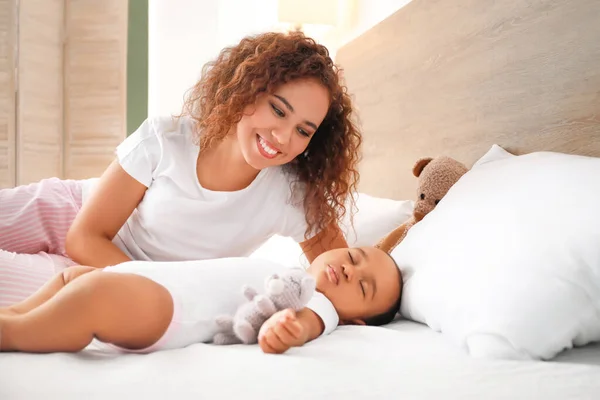 Young African-American woman and her sleeping baby on bed — Stock Photo, Image