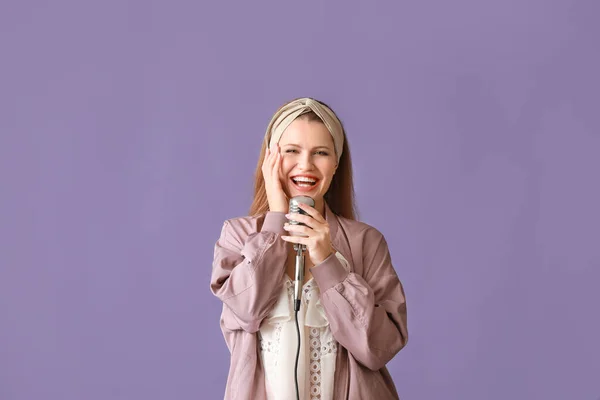 Schöne junge Sängerin mit Mikrofon auf farbigem Hintergrund — Stockfoto