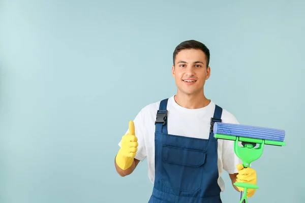 Young man with mop showing thumb-up on color background — Stock Photo, Image