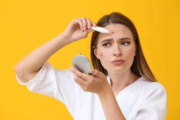 Retrato de mujer joven usando remedio para el acné sobre fondo de color — Foto de Stock