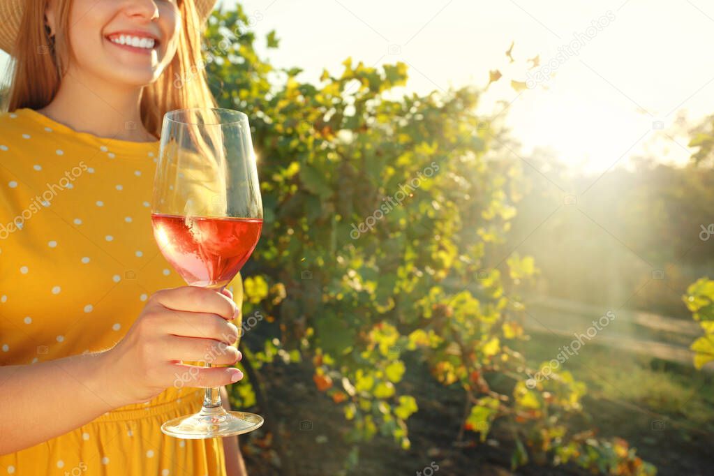 Young woman with glass of tasty wine in vineyard