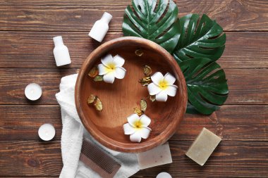Ahşap zemin üzerinde bir kase su, çiçek ve kozmetik içeren güzel bir spa kompozisyonu.