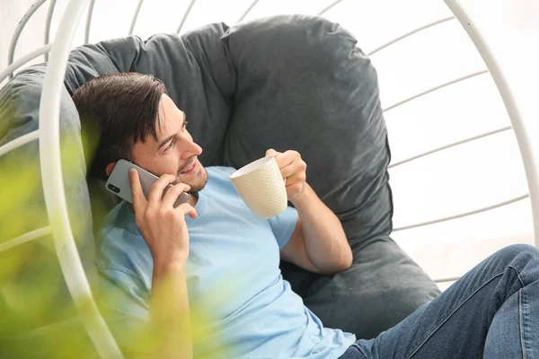 Snygg man dricker kaffe när han pratar i telefon hemma — Stockfoto