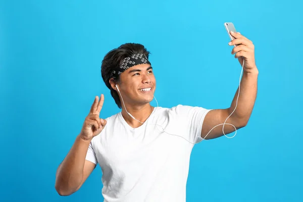 Retrato de bonito ásia homem ouvindo música enquanto tomando selfie no cor de fundo — Fotografia de Stock