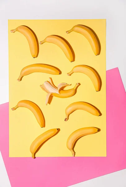 Banana sbucciata tra quelle non pelate su sfondo a colori. Concetto di unicità — Foto Stock
