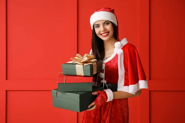 Hermosa mujer joven en traje de Santa Claus y con regalos contra la pared de color —  Fotos de Stock