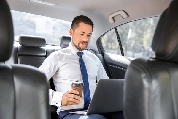 Uomo d'affari di successo con computer portatile bere caffè in auto moderna — Foto Stock