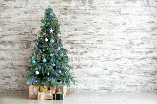 Gedecoreerde kerstboom en geschenken in de buurt van houten muur — Stockfoto