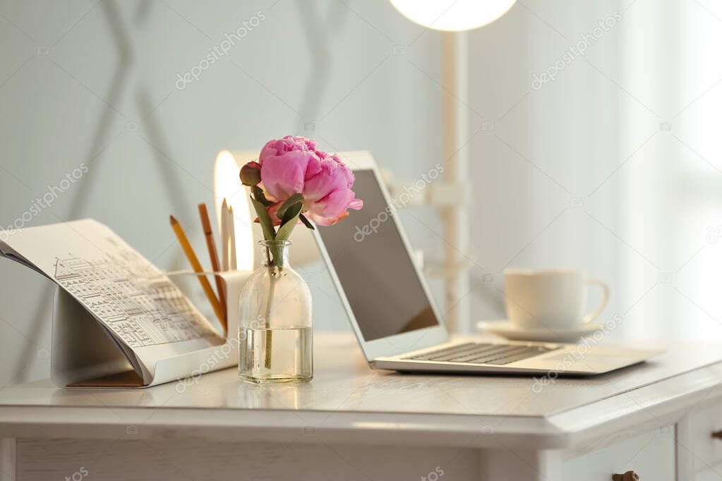 Vase with beautiful flowers and laptop on table in room