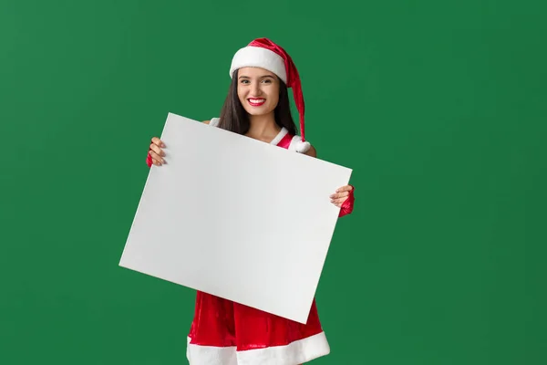 Hermosa mujer joven en traje de Santa Claus y con cartel en blanco sobre fondo de color Imagen de stock