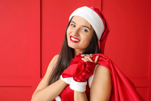 美丽的年轻女子，带着圣诞老人的包靠近彩墙 — 图库照片