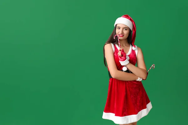 Hermosa mujer joven en traje de Santa Claus y con bastones de caramelo en el fondo de color —  Fotos de Stock