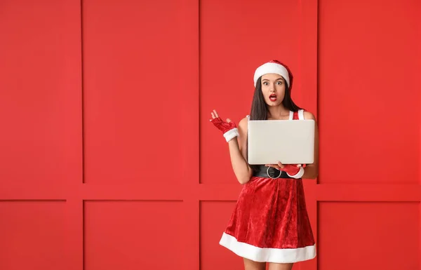 Bella giovane donna in costume di Babbo Natale e con computer portatile su sfondo a colori — Foto Stock