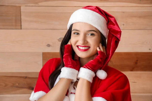 Mooie jonge vrouw in Santa Claus kostuum op houten achtergrond — Stockfoto