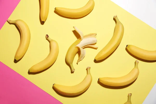 Banana sbucciata tra quelle non pelate su sfondo a colori. Concetto di unicità — Foto Stock