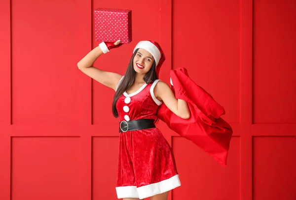 美丽的年轻女子，带着圣诞老人的包靠近彩墙 — 图库照片