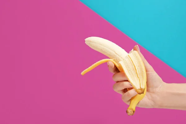 Mano femminile con banana sbucciata matura su sfondo colore — Foto Stock