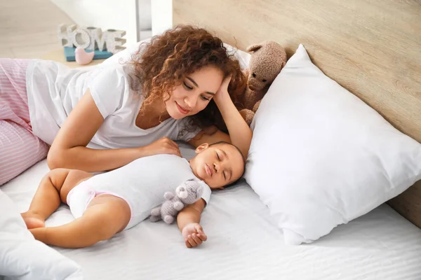 Young African-American woman and her sleeping baby on bed — Stock Photo, Image