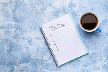 Empty to do list and cup of coffee on color background