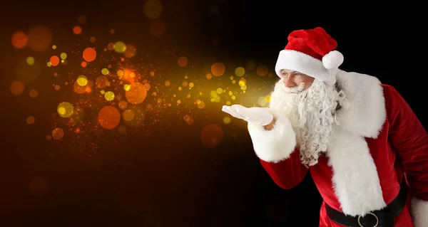 Santa Claus soplando luces brillantes sobre fondo oscuro —  Fotos de Stock