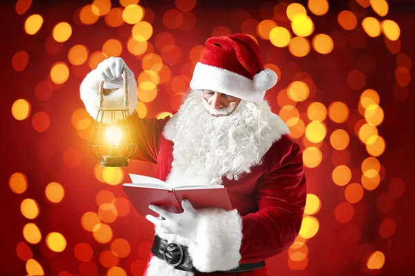 Santa Claus with lantern and book on color background with glowing lights — Stock Photo, Image