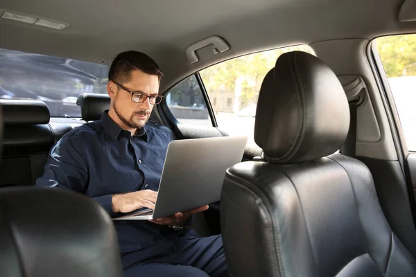 Erfolgreicher Geschäftsmann mit Laptop im modernen Auto — Stockfoto