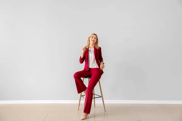 Beautiful stylish businesswoman sitting on chair against light wall — Stock Photo, Image