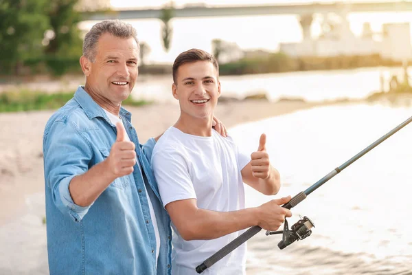 Молодой человек и его отец рыбачат на реке — стоковое фото