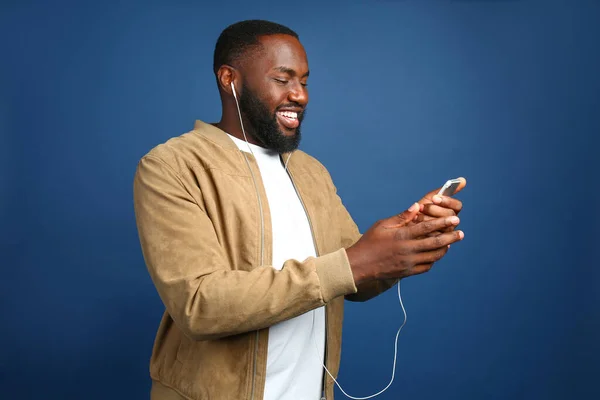 Happy African-American man listening to music on color background — Stock Photo, Image