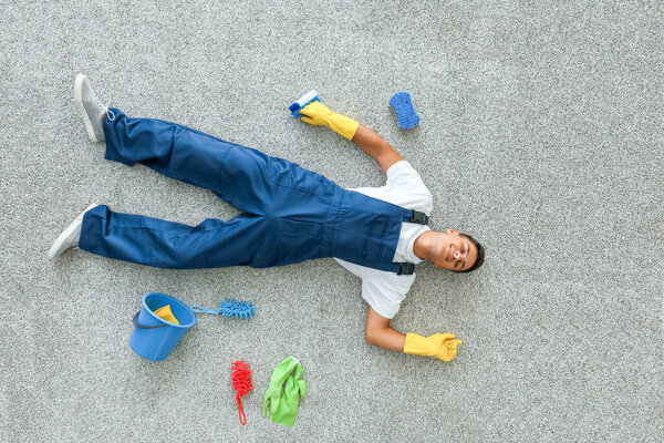 Уставший молодой человек лежит на полу после уборки квартиры, вид сверху
