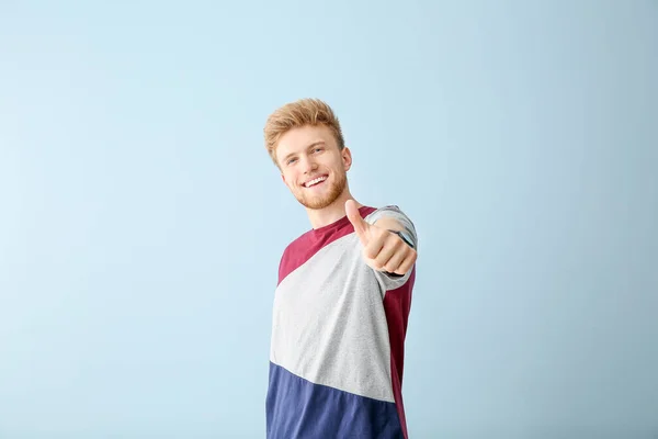 Portrait of young man showing thumb-up gesture on color background — Stock Photo, Image