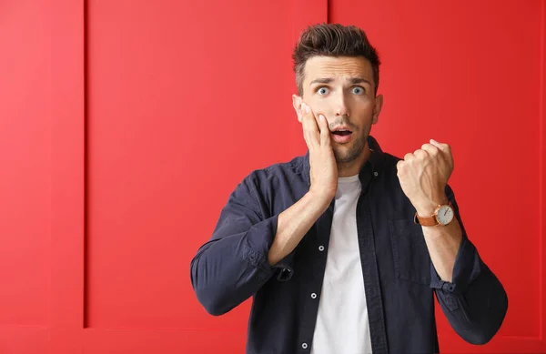 Gestresster junger Mann mit Uhr auf farbigem Hintergrund — Stockfoto
