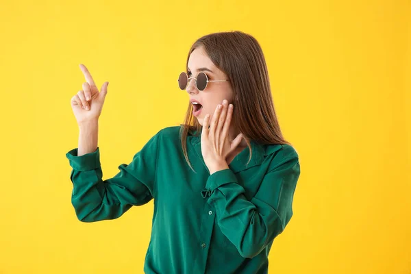 Surprised young woman pointing at something on color background — Stock Photo, Image