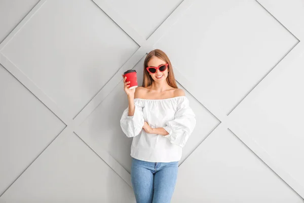 Krásná mladá žena s kávou na světlém pozadí — Stock fotografie