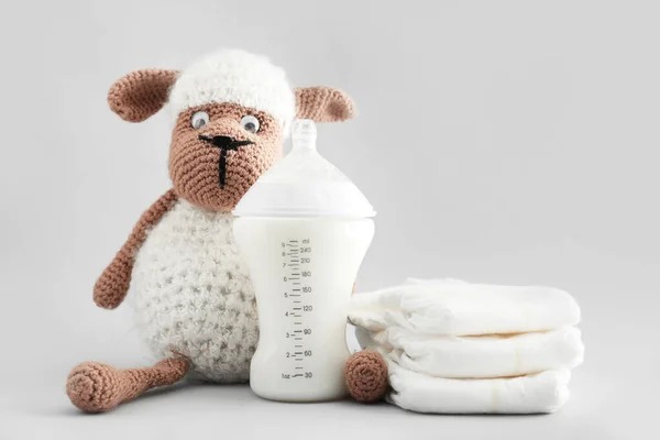 Бутылка молока для малыша с игрушками и подгузниками на сером фоне — стоковое фото