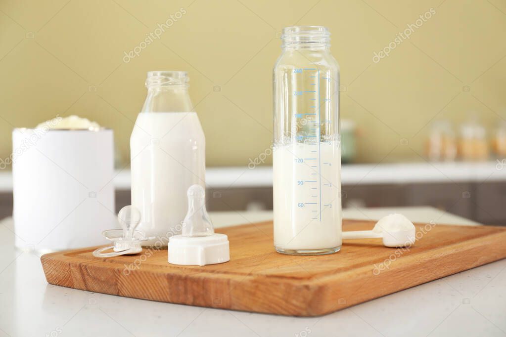 Bottles of baby milk formula with pacifier on table in kitchen