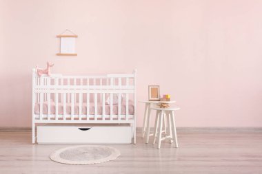 Çocuk odasının içindeki renkli duvarın yanında masası olan şık bir bebek yatağı.
