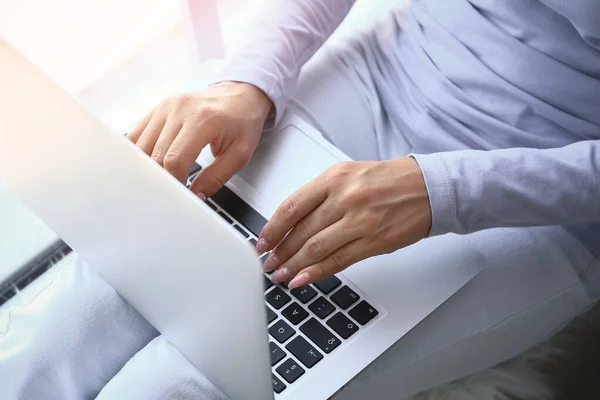 Young woman working on laptop near window — Stock Photo, Image