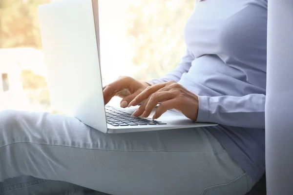 Young woman working on laptop near window — Stock Photo, Image