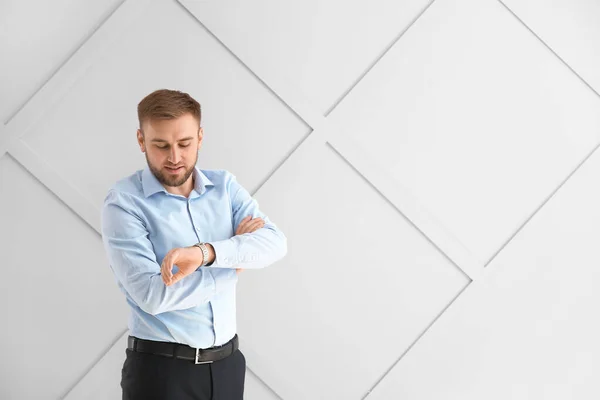 Portrait of handsome businessman looking at watch on light background — Stock Photo, Image