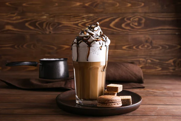 Glass of tasty frappe coffee with sweets on wooden table — Stock Photo, Image