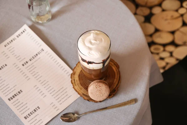 Glass of tasty frappe coffee with menu on table in cafe — Stock Photo, Image