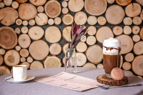 Glass of tasty frappe coffee with menu on table in cafe — Stock Photo, Image