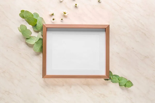 Empty frame with eucalyptus and flowers on light background