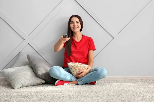 Mujer joven con palomitas de maíz viendo película cerca de la pared gris — Foto de Stock