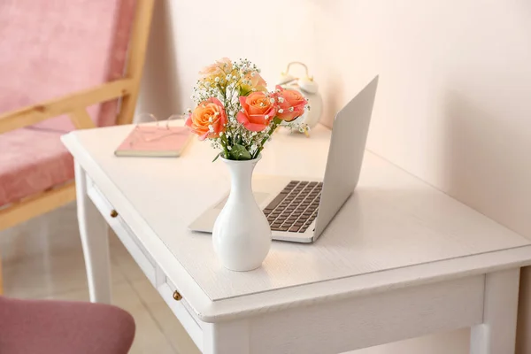 Mooi boeket in vaas en laptop op tafel in de kamer — Stockfoto
