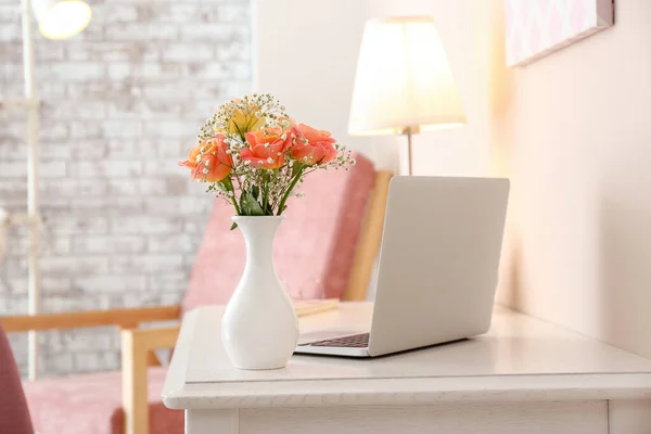 Vacker bukett i vas och laptop på bordet i rummet — Stockfoto