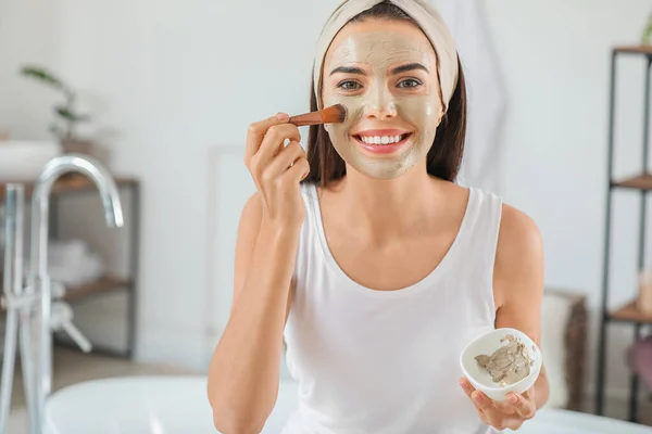 Beautiful young woman applying facial mask at home — Stock Photo, Image