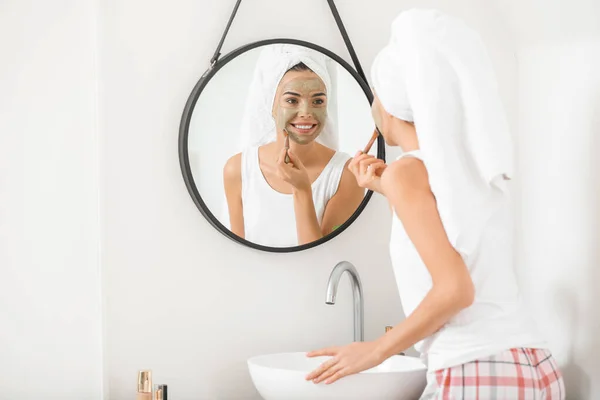 Beautiful young woman applying facial mask at home — Stock Photo, Image