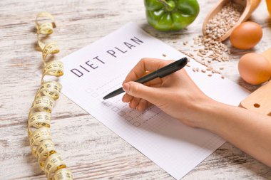 Woman writing something on sheet of paper with diet plan